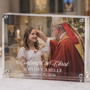 May include: A rectangular clear acrylic photo block featuring a printed image of a religious confirmation ceremony. The text reads Confirmed in Christ, SOPHIE CAMILLE, and January 31, 2026. The block is secured with four silver-toned metal corner screws.