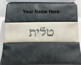 May include: A dark gray zippered bag with a white stripe across the center. The bag has the text "Your Name Here" at the top and Hebrew text embroidered on the white stripe. The bag is rectangular.