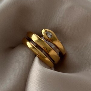 May include: Gold snake ring with a clear rhinestone on the head. The ring is made of three bands that wrap around the finger.
