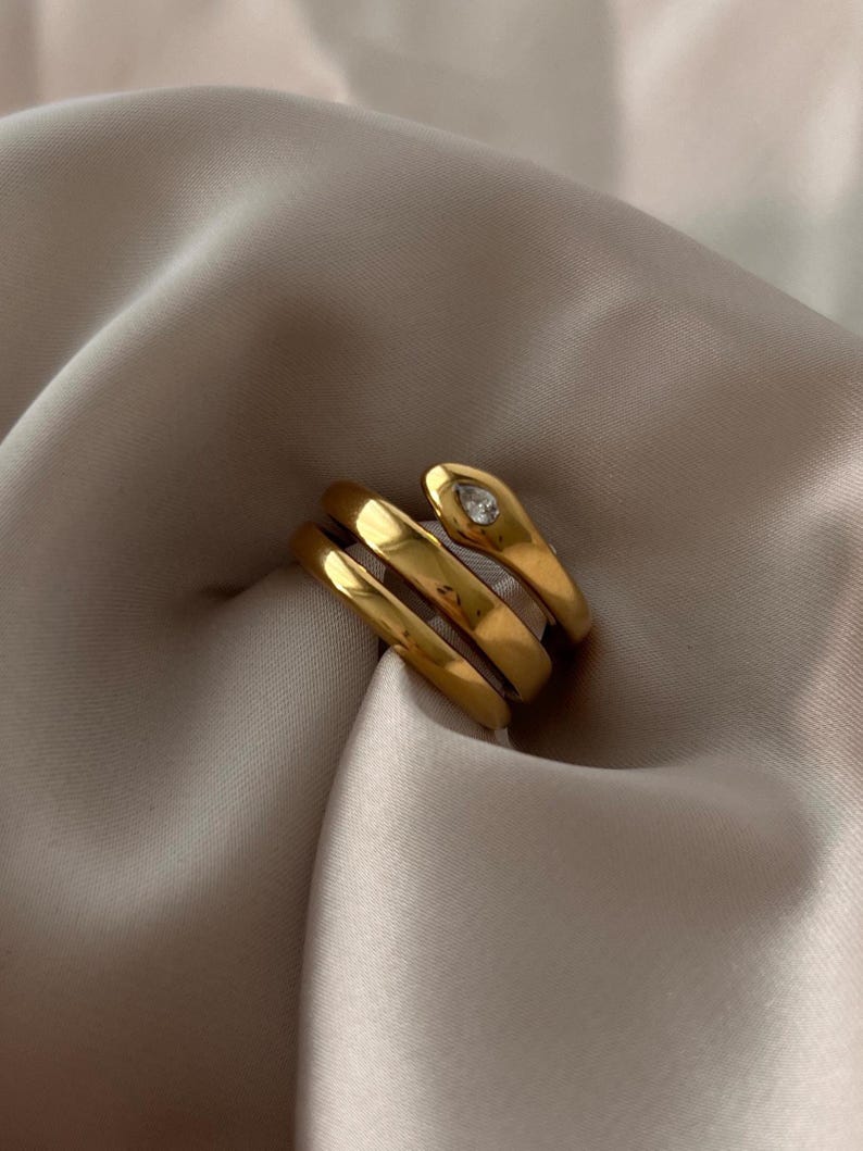May include: Gold snake ring with a clear rhinestone on the head. The ring is made of three bands that wrap around the finger.