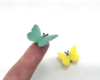 Peut inclure: Deux petites figurines de papillons, l'une d'une couleur vert menthe translucide et l'autre d'une couleur jaune vif unie. Chaque papillon présente des ailes délicates et de fines antennes noires, avec une finition lisse et un design simple.