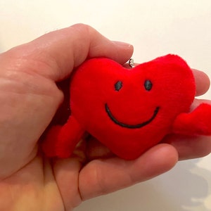 May include: A red plush heart-shaped keychain with a smiling face and two arms.