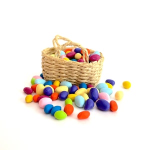 May include: A wicker basket overflowing with colorful pastel Easter eggs. The basket is tipped over, spilling the eggs onto a white surface.