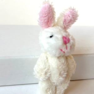K&ouml;nnte beinhalten: Ein kleiner wei&szlig;er Pl&uuml;schhase mit rosa Ohren. Der Hase hat schwarze Augen und eine rosa Nase.