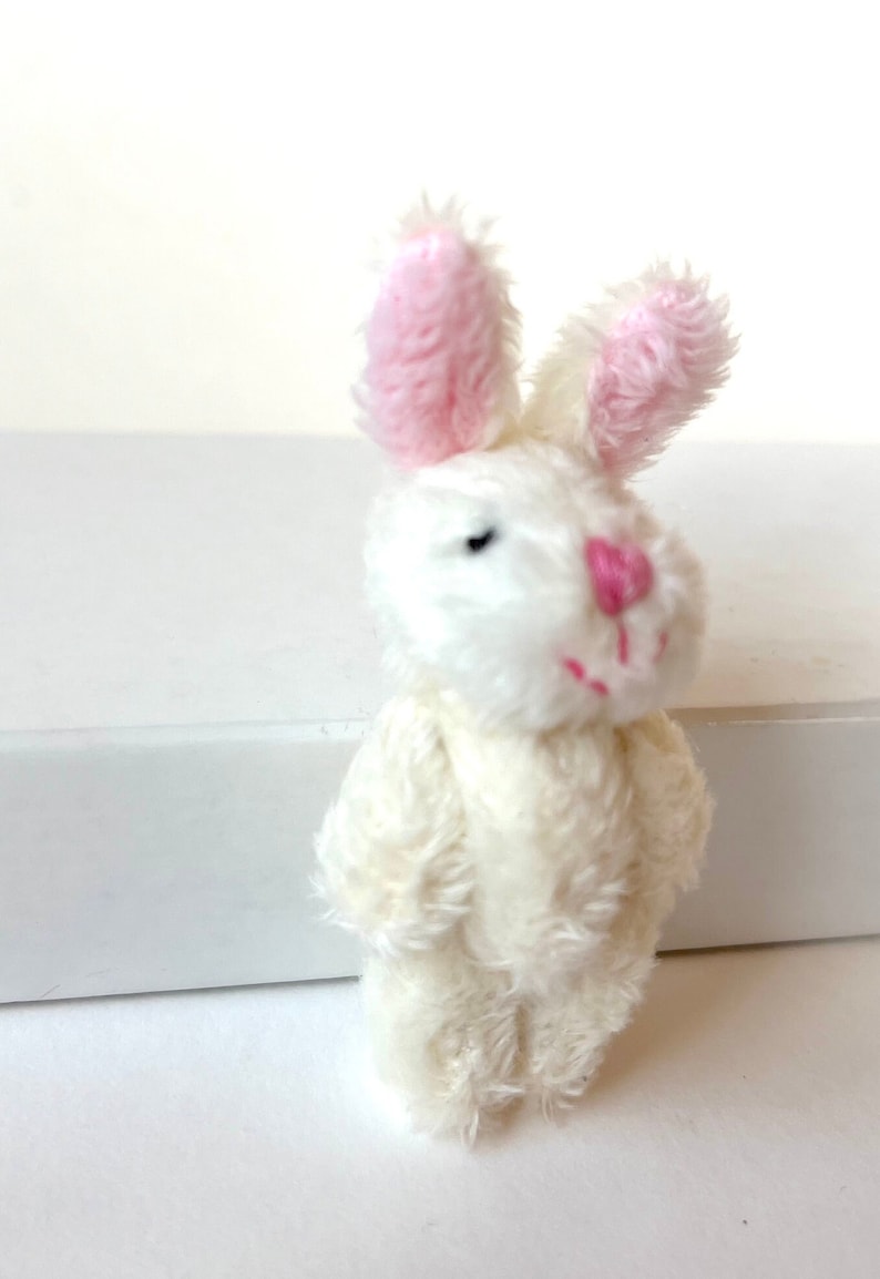 K&ouml;nnte beinhalten: Ein kleiner wei&szlig;er Pl&uuml;schhase mit rosa Ohren. Der Hase hat schwarze Augen und eine rosa Nase.