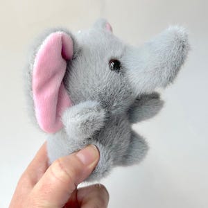 May include: A gray plush elephant toy with a pink ear. The elephant has a soft, fuzzy texture and a sweet expression.