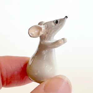 May include: A small, gray ceramic figurine of a mouse standing on its hind legs with its front paws raised. The mouse has a pink nose and black eyes.