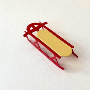 May include: A red metal sled with a cream-colored seat. The sled is a miniature version of a traditional sled.