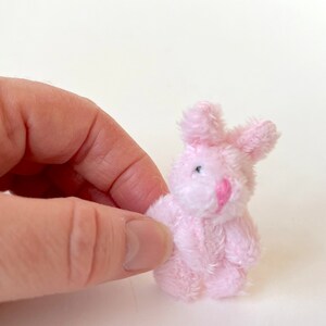 May include: A small pink plush bunny rabbit toy. The bunny has a white face with black eyes and a pink nose.