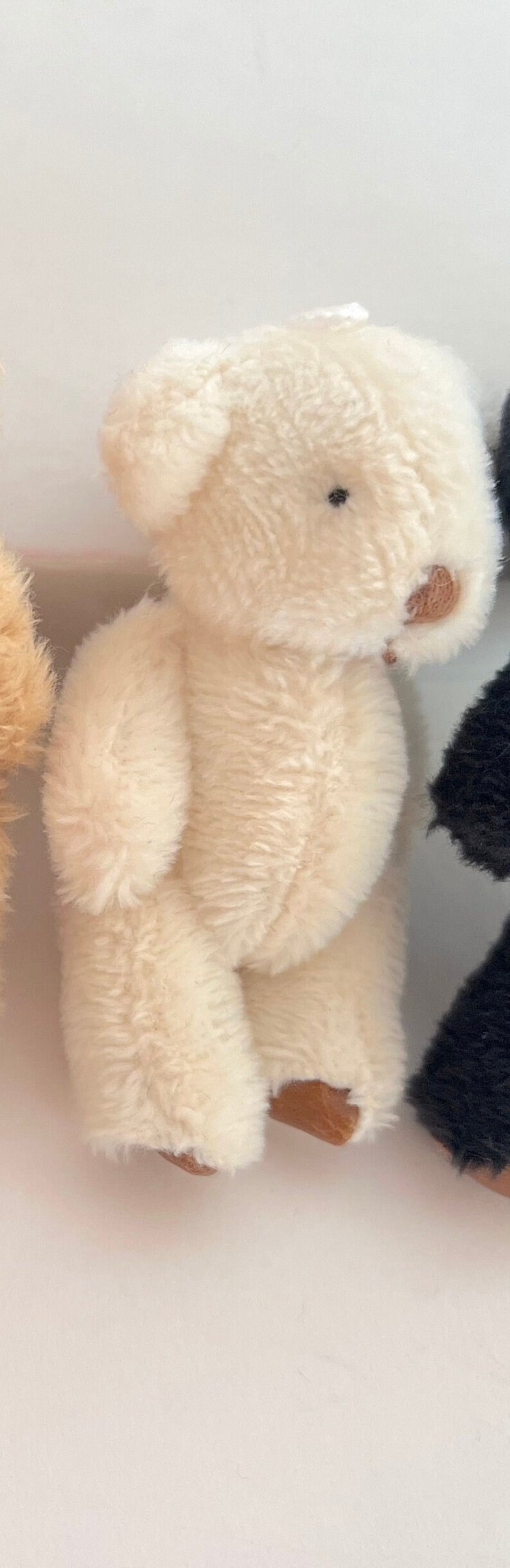 May include: A small, white, plush teddy bear with brown accents. The bear is sitting on a white surface.