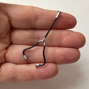 May include: Miniature black and silver stethoscope. The medical instrument has a Y-shaped design with a long, straight handle and two curved ear tubes. The ends of the tubes and the handle are silver.