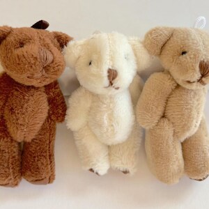 May include: Three small plush teddy bears. The bear on the left is brown, the middle bear is white, and the bear on the right is light brown.