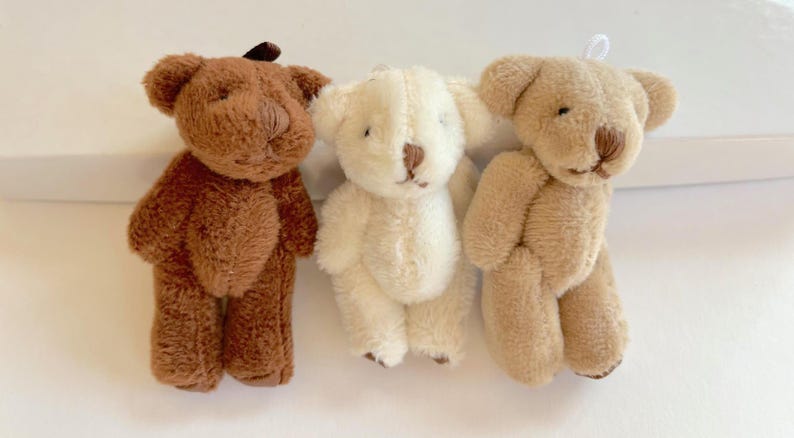 May include: Three small plush teddy bears. The bear on the left is brown, the middle bear is white, and the bear on the right is light brown.
