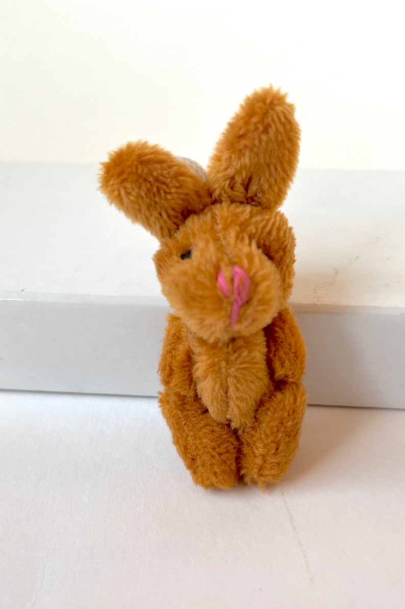 May include: A small brown plush bunny rabbit with pink nose and black eyes. The bunny is sitting with its legs crossed.