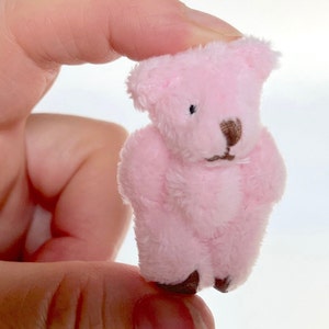 May include: A small pink teddy bear with brown eyes and a brown nose. The bear is made of soft, plush fabric.