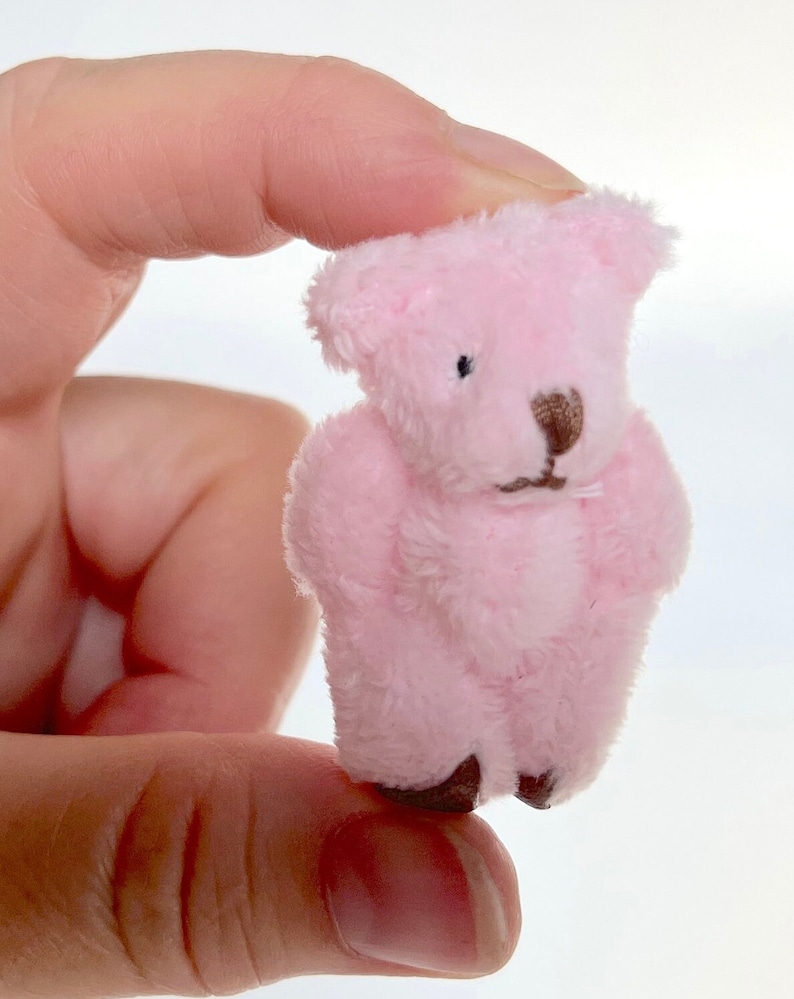 May include: A small pink teddy bear with brown eyes and a brown nose. The bear is made of soft, plush fabric.