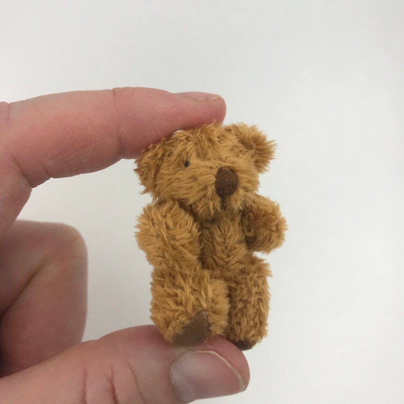 May include: A small, brown teddy bear with a fuzzy texture. The bear is sitting up with its arms and legs slightly outstretched.