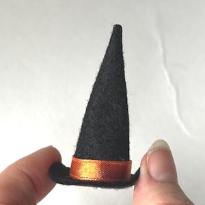 May include: A small black witch's hat with a conical crown and a broad brim. It has a bright orange ribbon encircling the base. This Halloween-themed item is likely for a doll or craft project, and is a fun accessory.