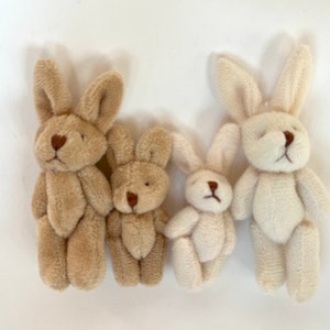 May include: Four plush bunny toys, two brown and two white, are arranged in a row. The bunnies are all standing upright with their ears perked up.