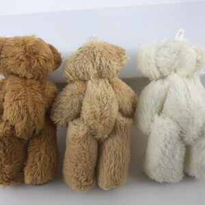 May include: Three plush teddy bears, one brown, one beige, and one white, standing in a row.