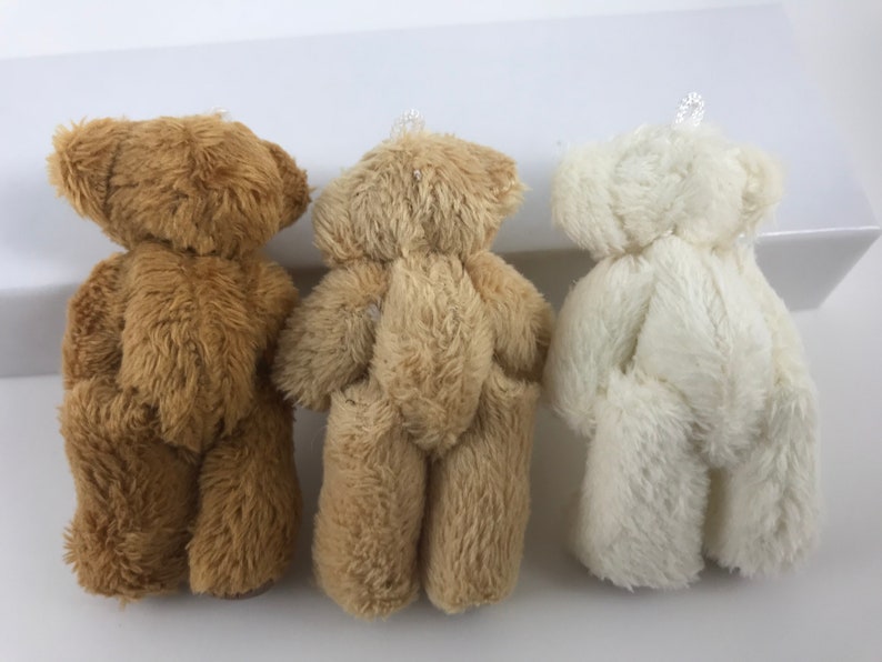 May include: Three plush teddy bears, one brown, one beige, and one white, standing in a row.