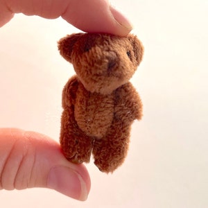 May include: A small brown teddy bear with a fluffy texture. The bear is standing upright with its arms by its side.