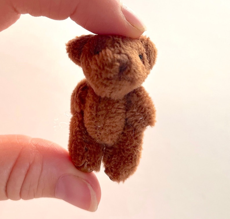 May include: A small brown teddy bear with a fluffy texture. The bear is standing upright with its arms by its side.