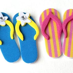 May include: Two pairs of flip-flops, one pair is blue with yellow flowers and the other pair is yellow and pink striped.