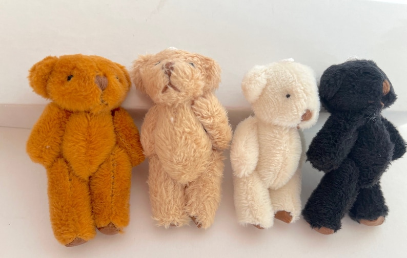 May include: Four small teddy bears in different colors: brown, beige, white, and black. The bears are all standing upright and have a simple design.