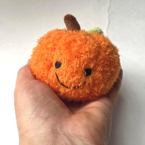 May include: A plush orange pumpkin with a smiling face, brown stem, and green leaf. The pumpkin is round and fluffy, perfect for fall decor or a child's toy.