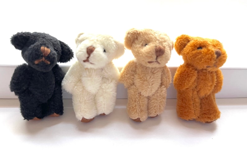 May include: Four small teddy bears in different colours: black, white, brown, and orange. The bears are all standing upright and have a simple, classic teddy bear design.