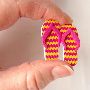 May include: A pair of pink and yellow flip-flop shaped buttons. The flip-flops have a chevron pattern.