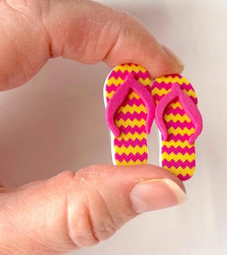 May include: A pair of pink and yellow flip-flop shaped buttons. The flip-flops have a chevron pattern.