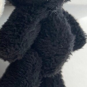 May include: A black plush toy bear with brown feet. The bear is standing on a white surface.