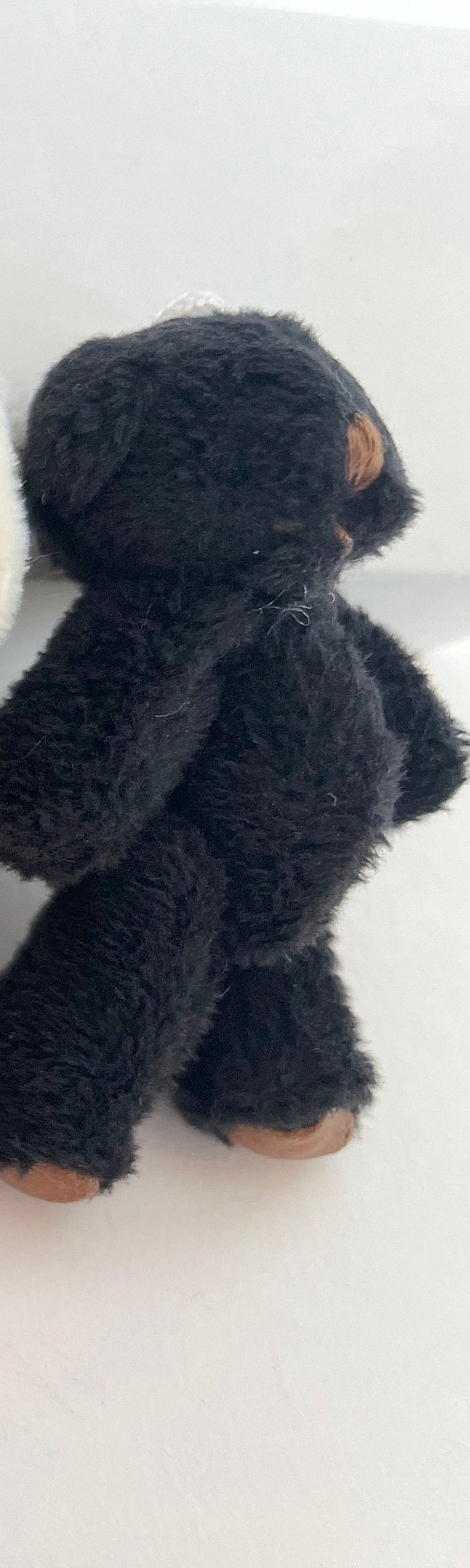 May include: A black plush toy bear with brown feet. The bear is standing on a white surface.