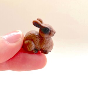 Puede incluir: Una pequeña figurita de conejo marrón con ojos negros. La figurita está hecha de plástico y tiene una textura peluda.