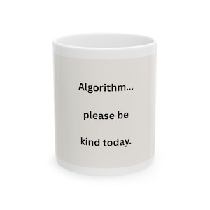 May include: A white ceramic mug featuring the black printed text "Algorithm... please be kind today." The mug has a cylindrical shape with a smooth, glossy finish and a simple, clean design, displaying the text clearly on the front surface.