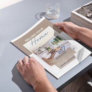 May include: A tan and white brochure with the text "Selling Your Home" in blue script. The brochure is open to a page with a photo of a modern kitchen and dining room. The text "Presented By: Emily Tom Your Real Estate Mom" is in a blue rectangle at the bottom of the page.