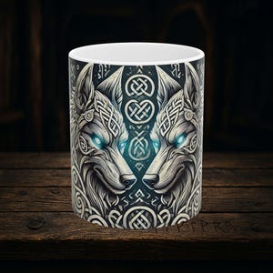 May include: White ceramic mug with a black and white illustration of two wolf heads facing each other. The wolf heads are surrounded by intricate Celtic knotwork.