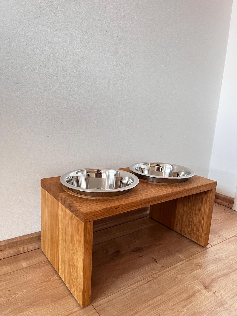 Puede incluir: Un comedero de madera para mascotas con dos cuencos de acero inoxidable. El comedero es de madera marr&oacute;n claro y tiene un dise&ntilde;o simple y moderno. Los cuencos son redondos y brillantes, ideales para alimentar a las mascotas.