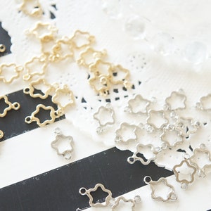 以下が含まれることがあります： 星型の金属製コネクターチャームが2つの山になって置かれている。片方の山は金色、もう片方は銀色である。