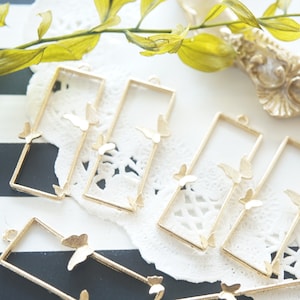 Puede incluir: Marcos de metal dorado con recortes de mariposa. Los marcos son rectangulares y tienen un agujero en la parte superior para colgar.