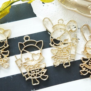 May include: Four gold-colored metal charms featuring cartoon characters. Each charm has a black outline and a white interior. The characters are wearing outfits with black and white details.