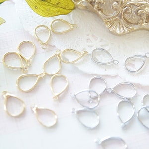 Puede incluir: Una colección de hallazgos para pendientes en forma de lágrima de oro y plata. Los hallazgos están dispuestos sobre una superficie blanca con una superposición de encaje.