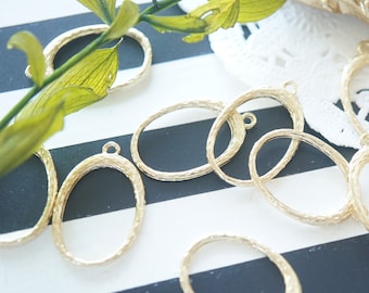 May include: A set of ten gold oval-shaped metal pendant trays with a textured surface. The trays have a loop at the top for hanging.