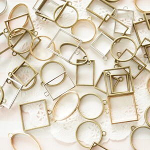 May include: A selection of metal bezel pendants in diverse shapes, such as circles, squares, and rectangles. The pendants have a vintage brass and silver finish, with clear glass inserts. These jewellery findings are suitable for crafting.