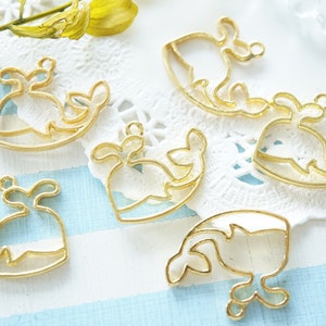 Può includere: Sei ciondoli a forma di balena in metallo dorato con un design aperto. I ciondoli sono su una superficie di pizzo bianco.