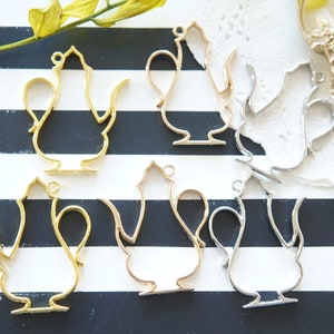 Puede incluir: Seis colgantes de metal en forma de tetera, en oro, plata y oro rosa, sobre una superficie rayada en blanco y negro. Los colgantes tienen forma de tetera con asa y pico.