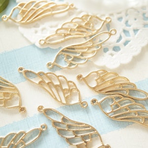 May include: A collection of gold-toned metal angel wings with a delicate, intricate design. The wings have a heart-shaped cutout at the center and are perfect for crafting jewelry or adding a touch of whimsy to projects.