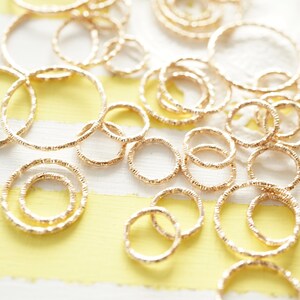 May include: A collection of gold-toned, textured metal rings of varying sizes. The rings are arranged on a yellow and white striped surface.